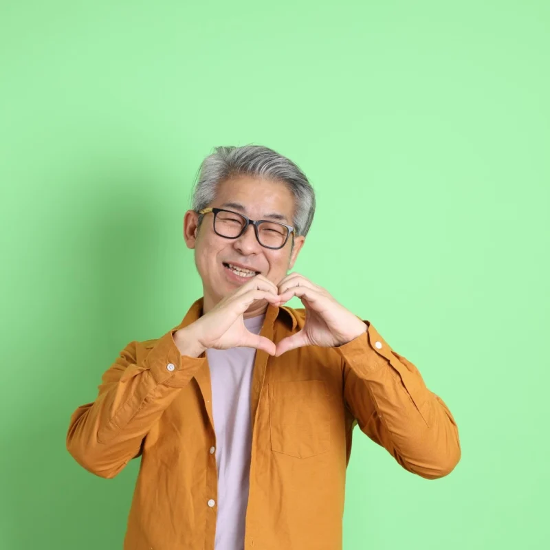 Happy asian man smiling at camera and making love heart symbol with his hands